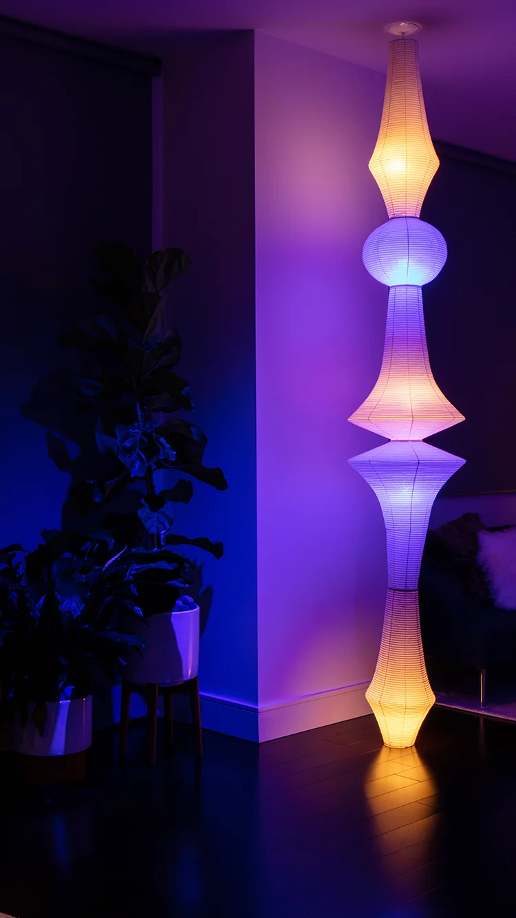 A modern glass-walled home illuminated at night with warm interior lighting, contrasting against the dark blue evening sky, showcasing a blend of ambient and accent lighting.